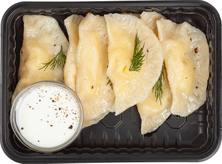 Dumplings with sour cream in a disposable rectangular plastic black lunch box top view on a white backgroundの写真素材