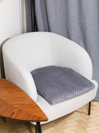 A stylish white chair featuring a soft gray cushion is comfortably positioned next to a lovely wooden table, enhancing the overall decorの写真素材
