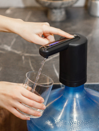 A person is actively pouring water into a glass using a water dispenser machine, ensuring they have enough hydration for their drinkの写真素材