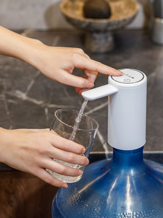 An individual is meticulously pouring fresh water from a plastic water bottle into a clear glass, ensuring no spills occurの写真素材