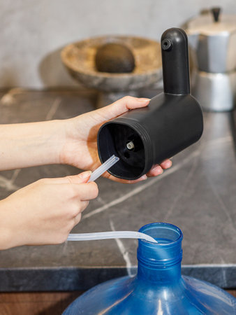 A person is meticulously filling a water bottle using a straw to ensure the liquid flows smoothly into the container without spillsの写真素材