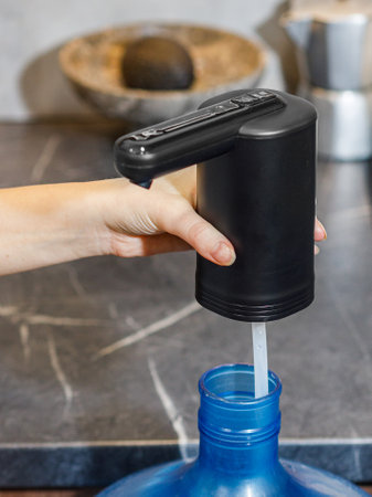 A person is carefully pouring water from a source into a blue bottle, ensuring that the liquid fills it adequately without spilling overの写真素材