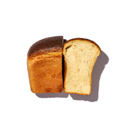 A freshly baked loaf of bread has been sliced neatly in half and is placed against a clean white...