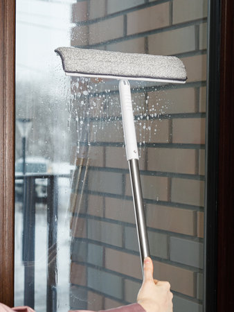 A person is diligently cleaning a window using a squeegee to ensure it is spotless and shiny, enhancing the view outdoorsの写真素材