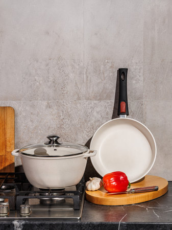 In a cozy kitchen, a pot and a pan are resting on the stove, while a cutting board adorned with fresh vegetables sits nearby, ready for cookingの写真素材