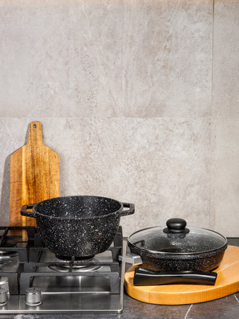 On a stove, there are two black pots that are placed side by side next to a wooden cutting board, ready for cooking and food preparationの写真素材