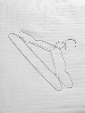 Two white clothes hangers are lying flat on a white cloth surface, creating a subtle contrast that enhances their presenceの写真素材