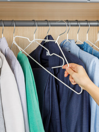 A person is carefully reaching into their closet to pick up a shirt that they have stored away for different occasionsの写真素材