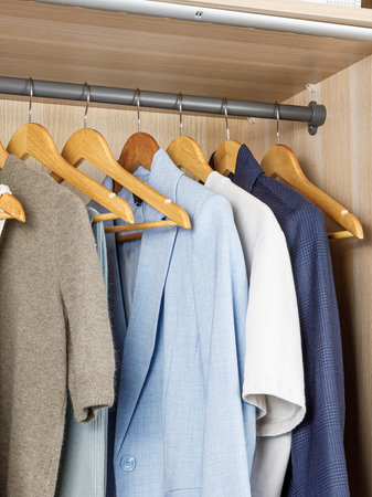 A closet that is filled with various clothes neatly hanging on sturdy wooden hangers, showcasing an array of garments and stylesの写真素材