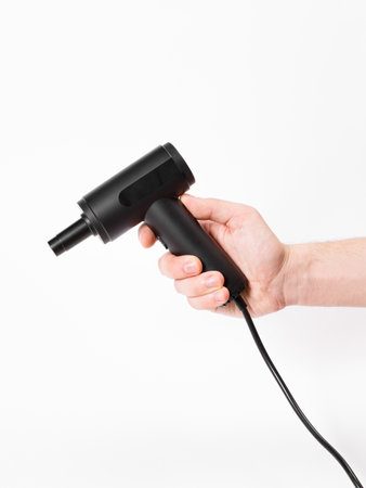 A person is holding a black hair dryer firmly in their hand, showcasing the tool that is commonly used for styling hairの写真素材