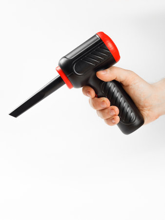 A person is firmly holding a black and red dust blower in their hand, showcasing an essential tool...