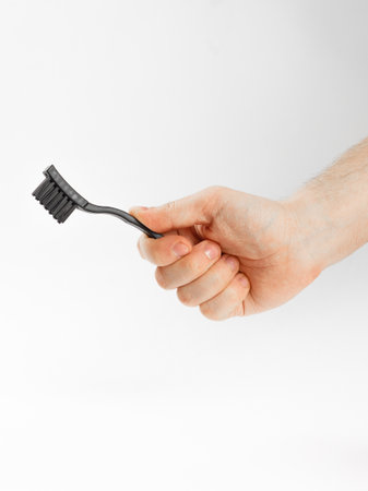 A hand is firmly holding a black toothbrush against a clean white background, making it visually stand out in this simple yet effective sceneの写真素材