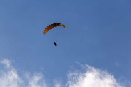 Paraglider in flight with lots of bright clouds and blue sky seen from belowの写真素材