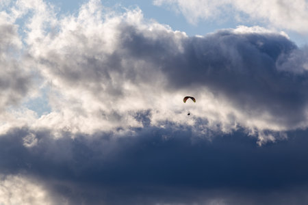 Paraglider in flight backlit with lots of bright clouds and blue skyの写真素材