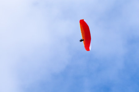 Paraglider in flight with lots of bright clouds and blue sky seen from belowの写真素材
