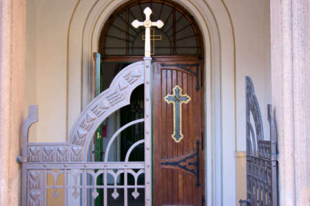 Entrance to an Orthodox church showing two Greek Orthodox crosses, a gate, and a partially opened door の写真素材
