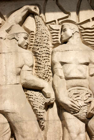 On the facade of a building in Budapest, Hungary, a Socialist realist rendering of two fishermen with net and basket of fish の写真素材