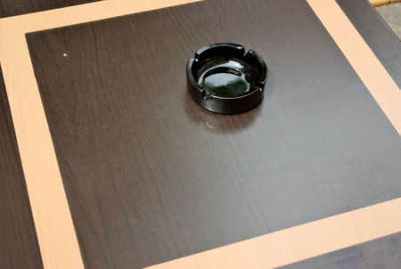 A black ceramic ashtray sits alone on a brown cafe tableの写真素材