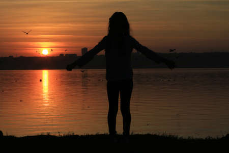 Silhouette on the beach at sunset. Silhouette of girl jumping in sunset. Girl standing on the beach at sunset.の写真素材