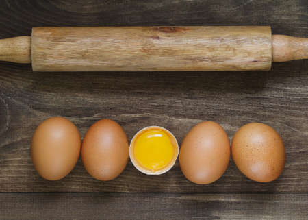 Top view on fresh eggs in a row and rolling pin on a wooden table. Cooking concept.の写真素材