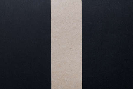 A black sheet of paper divided in half by a vertical stripe of kraft paper. Abstract composition.の写真素材