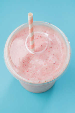 Top view of a strawberry smoothie in a plastic cup with a straw on a blue background. Pastel color. Summer and healthy lifestyle concept.の写真素材