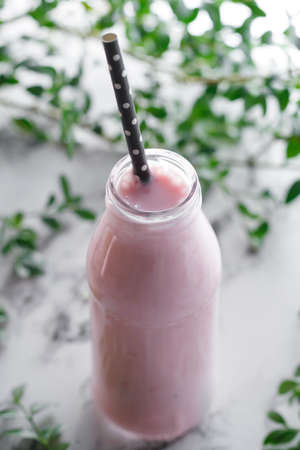 Close-up of bottle with a pink fresh berry smoothie on white marble table. View from above.