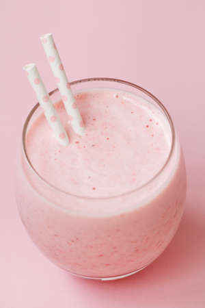 Strawberry pink smoothie in a glass with a straw on a pink background. Summer and healthy lifestyle concept.の写真素材