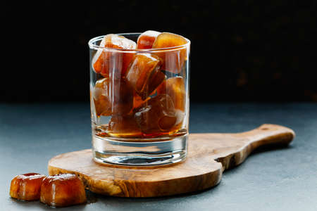 Coffee ice cubes in a glass on a wooden board on a black table.の写真素材