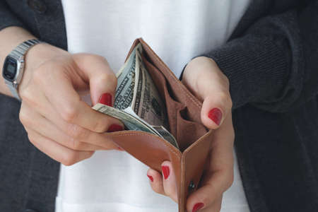 The girl pays in the shop. Hands holding an open leather orange slim purse with cash dollars.