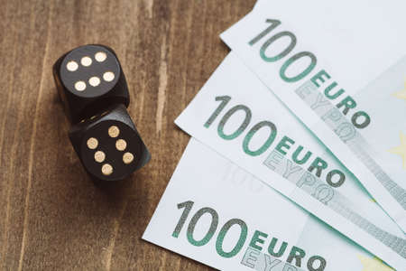 Playing for money. Black dice and euro on a wooden table.の写真素材