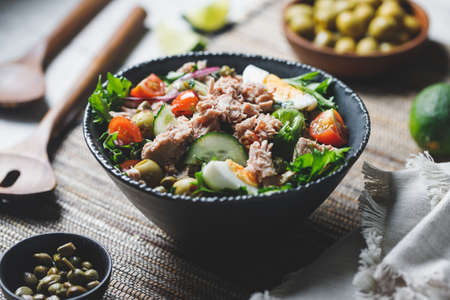 Canned tuna salad with fresh vegetables, capers and olives in a black bowl. Healthy lunch or dinner.の写真素材