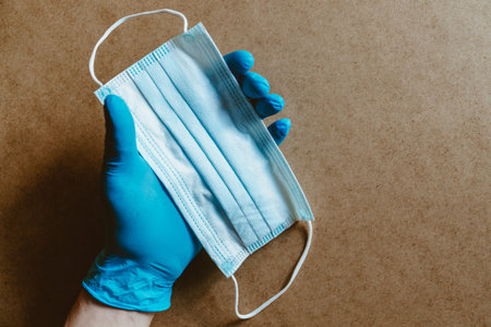 Hand in blue rubber gloves holds a medical mask. Health care and antivirus protection concept, top view.の写真素材