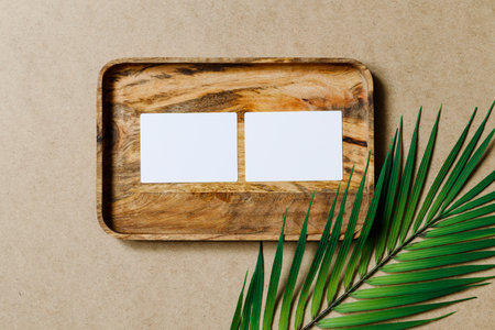 Top view of two blank paper sheet cards on a wooden tray with palm leaf. Tropic mockup for business template, copy space.の写真素材