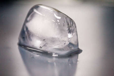 An ice cube makes water on a smooth, gray-colored surface.の写真素材