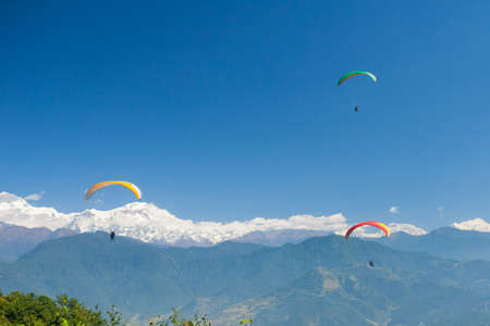 Tandem paragliders float over Nepal with the Annapurna Himalayas in the backgroundの写真素材