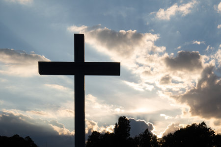 Christian cross silhouetted against the sunset and cloudsの写真素材