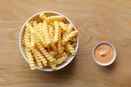 Bowl with french fried potatos and souce on a wooden table