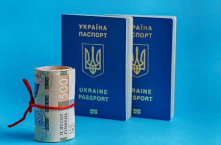 500 hryvnia roll wrapped in a red rope ribbon on the back plate 2 biometric passports of Ukraine on blue backgroundの写真素材