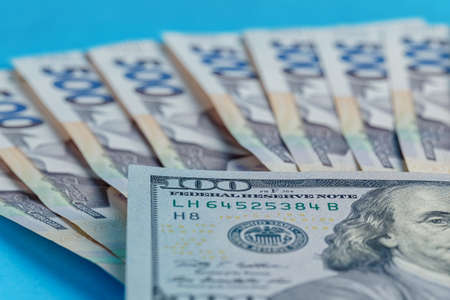 100 dollars banknote next to a lot of money 500 hryvnia lying on a blue background closeup dollar...