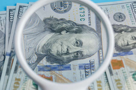 Deck of lying 100 dollars through a magnifier close-up on a blue backgroundの写真素材