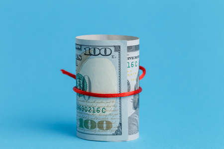 A roll of dollars wrapped in a red rope ribbon on blue background 100 dollarsの写真素材