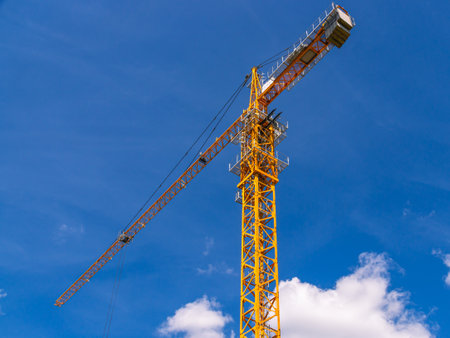 A tower construction crane on the background of a blue sky with clouds. Boom rotary crane with boom. Construction of apartment buildings in the city. Construction of high rise buildings.の写真素材