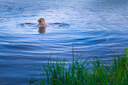 Evening swimming in the river. A woman with red hair is bathing in the river. Healthy outdoor recreation by the river. The surface of the water. Weekend in the country, in nature.の写真素材