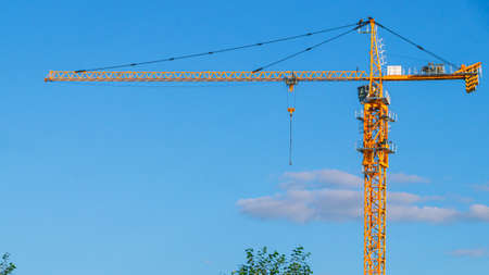 A tower construction crane on the background of a blue sky with clouds. Boom rotary crane with boom. Construction of apartment buildings in the city. Construction of high rise buildings.の写真素材