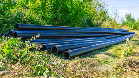 Large diameter plastic pipes for outdoor water supply. HDPE pipes lie in the field. Smooth black...
