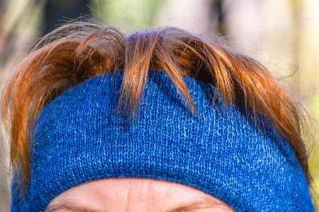 A walk through the autumn forest. A woman in a knitted bandage made of natural wool. A woman with red hair and a headband for keeping warm in cool weather. A walk in the city park in warm clothes.の写真素材