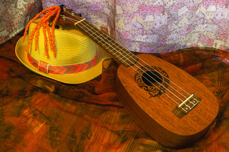 Hawaiian guitar for chord accompaniment of songs and solo performance. Miniature four-string ukulele. A ukulele and a hat on a brown background. A small musical string instrument.の写真素材