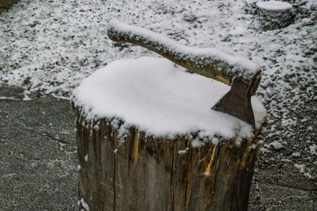 A snow-covered ax on a wooden block. Harvesting firewood for heating in the village in winter. Life in the countryside in winter.の写真素材