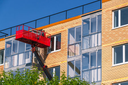 Construction lift for finishing works at height. A construction worker works in a cradle of a lifting mechanism at a height. High-rise works during the construction of a residential building.の写真素材